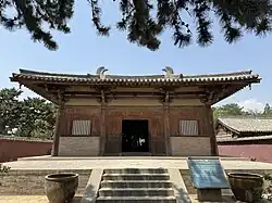 The Great Buddha Hall of Nanchan Temple. A small timber building with massive overhanging eaves with a bright blue sky behind it.