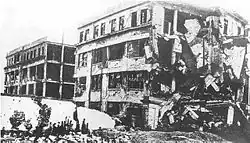 A black and white photo of the ruined headquarters of the Commercial Press, showing a four story building with much of its side wall collapsed