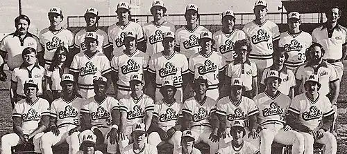 A black and white photograph of baseball players in uniforms and caps posed in three rows, standing, sitting in chairs, and sitting on a bench on a baseball field