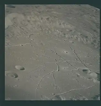 Eastern crater floor. The mare-type material on the floor contains radial cracks and concentric rilles. A dark-halo area is visible at the lower left corner. Low hills of material that resemble the central peak protrude through the smooth crater floor. Bright-halo craters are also evident. The "doughnut" filling of the crater at the left margin is a rare feature.[5]