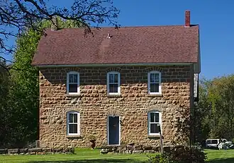 A simple two-story stone house with a gable roof