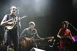 Four people performing instruments and singing into microphones