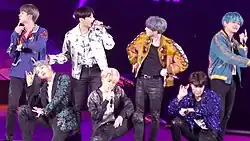 Seven men performing on stage against a purple background