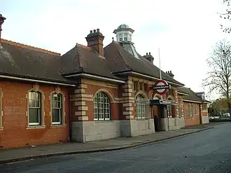 A red-bricked building with a sloping, black roof, four chimneys, and a sign that reads "UNDERGROUND" under a blue sky with white clouds