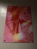 Art of two drag queens in pink lighting on a grey wall.