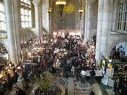 View of banking room in 2010. There is a crowd of people attending a fair in the middle of the banking room. Large windows are visible to the left.