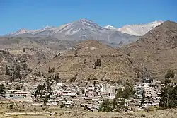 Several mountains, some snow covered, rise above a village in a valley