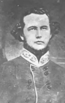 Black and white photo shows a clean-shaven, young man dressed in a gray military uniform with a bright-colored collar.
