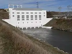 Powerhouse with tailrace canal running out of base; electrical transformers on canal bank at right