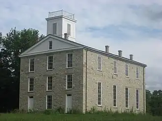 Three story gray rectangular building on a grassy hill