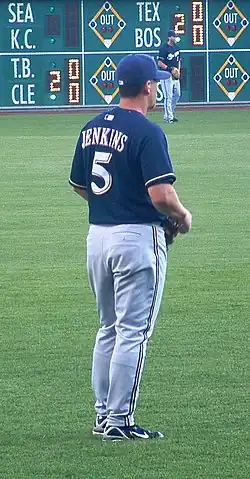 A man in a navy-blue baseball jersey and cap and gray baseball pants stands on a baseball field.