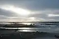 Sandy beach with sunbeams peeking through overcast sky
