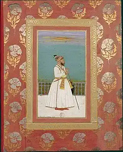 A bearded man facing right with a walking stick