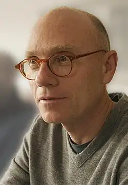 A bald man wearing glasses and a gray T-shirt looks off-screen.