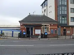 A red-bricked building with a rectangular, dark blue sign reading "KENTON STATION" in white letters all under a blue sky with white clouds