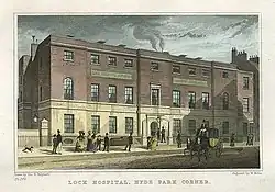 This image shows the London Lock Hospital from the street in the late 18th century. It is a red brick building in the Georgian style on a busy street.