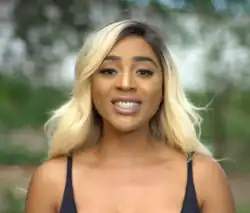 A woman wearing a black top, with black and blonde hair is smiling.