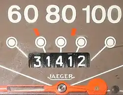 A strongly illuminated black surface with "60 80 100" on top in large white letters above a radial design. In the middle of the radial is "31412" in a recessed area on indicator wheels.