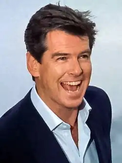 Smiling man with short, tousled hair, wearing white shirt open at collar, and black jacket.