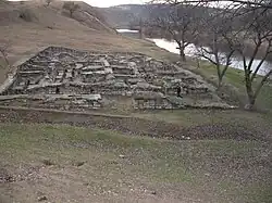 Large, low stone construction (with people walking past for scale) near a river