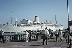 A passenger line at dock with pedestrians on the quay