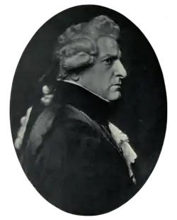 Right profile of stern-faced man in dark clothing with lacy shirt and cuffs, wearing a wig