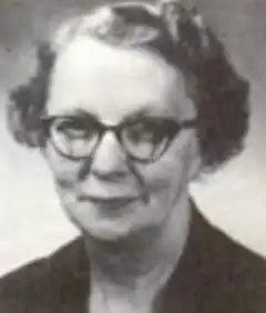 An older white woman wearing round glasses and a dark dress or jacket