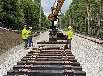 Workers using a machine to place wooden railway ties