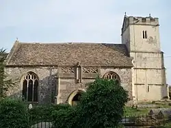 A stone church seen from the north with a central doorway surmounted by a pierced parapet, and to the right a battlemented tower