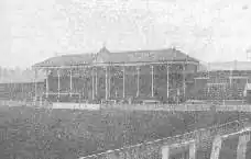 View towards one end of the ground, showing a roof, supported by several pillars and bearing a clock, covering the central part (behind the goal) of an otherwise open terrace